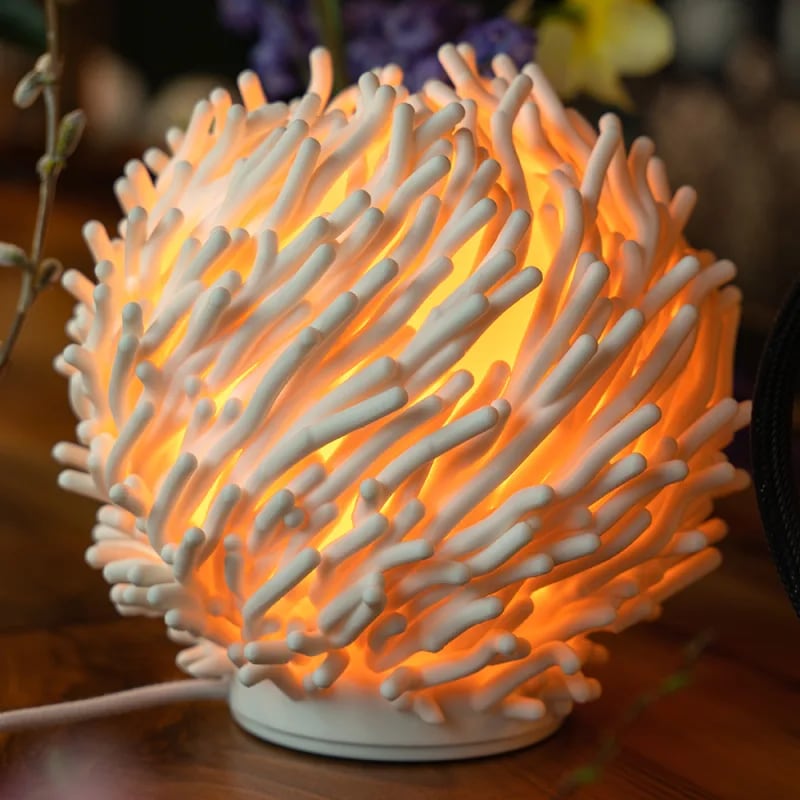 A lit Coral lamp on a wooden table, its white branches glowing orange from the light inside.