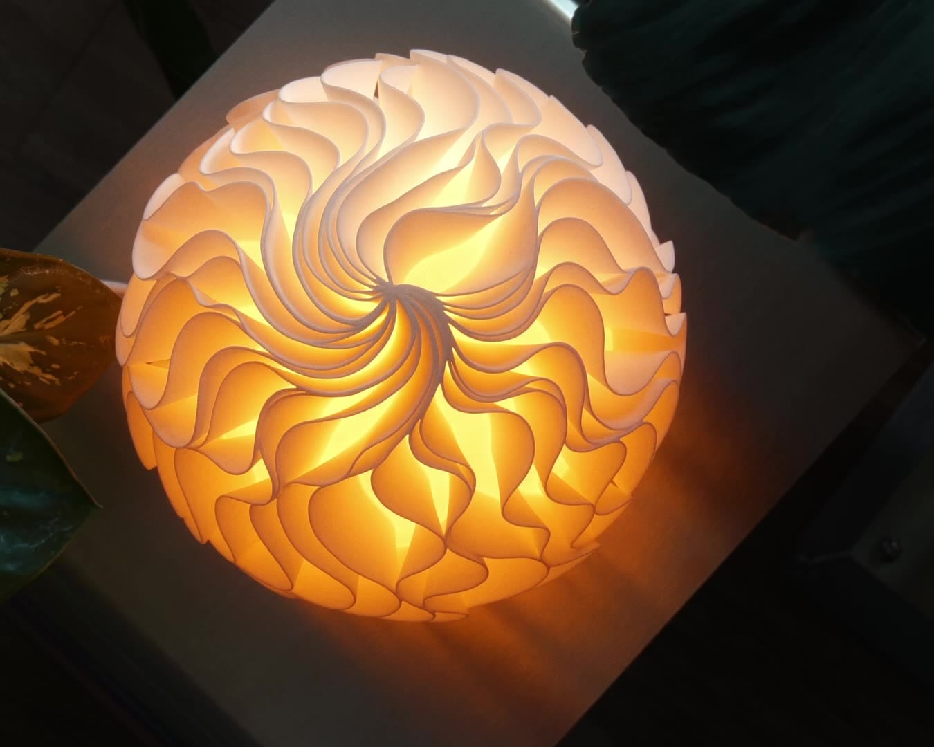 A lit Growth lamp seen from above: its ruffled fins spiral out from the middle of the top and glow orange.